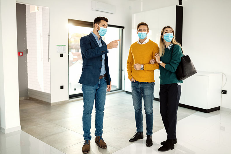 Real estate agent communicating with a couple while showing them a new apartment and wearing protective face mask due to COVID-19 pandemic.